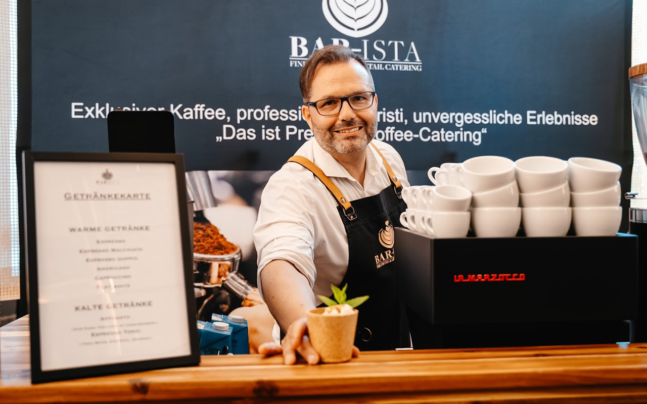 Der Barista reicht ein Getränk über die Theke | Kaffee-Catering - Messe